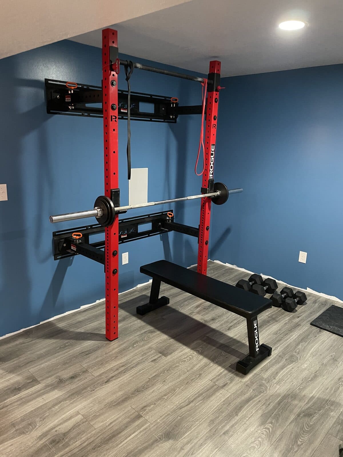 Basement home gym with red squat rack and rubber flooring