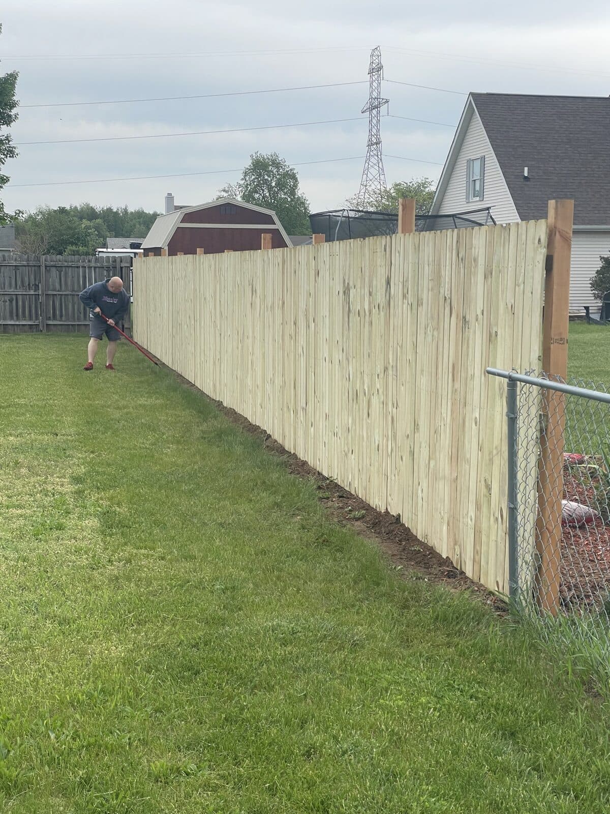 Privacy fence installation along property line, panels going up next to chain-link
